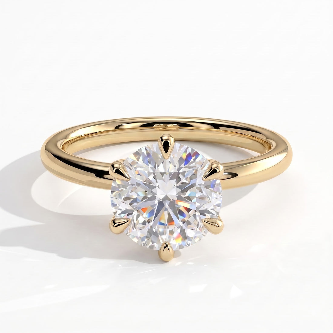 A classic solitaire engagement ring featuring a round brilliant-cut diamond set in a yellow gold four-prong setting, on a polished yellow gold band, shown on a clean white background with a soft shadow. 