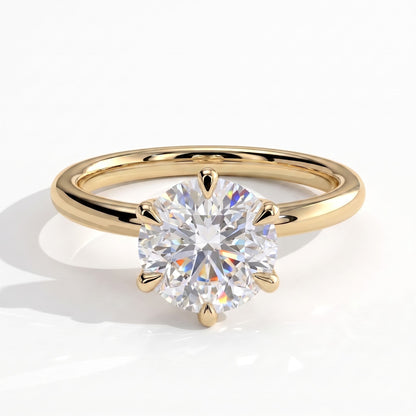 A classic solitaire engagement ring featuring a round brilliant-cut diamond set in a yellow gold four-prong setting, on a polished yellow gold band, shown on a clean white background with a soft shadow. 