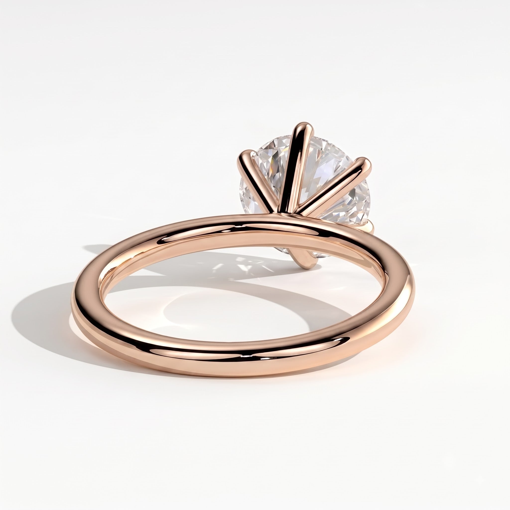 A rose gold solitaire engagement ring with a round brilliant-cut clear gemstone in a prong setting, shown on a clean white background with a soft shadow. 