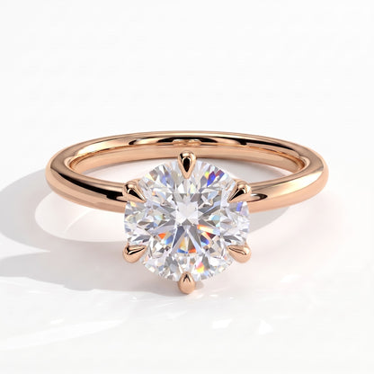 A rose gold solitaire engagement ring with a round brilliant-cut diamond set in a six-prong setting, shown on a clean white background with a soft shadow. 