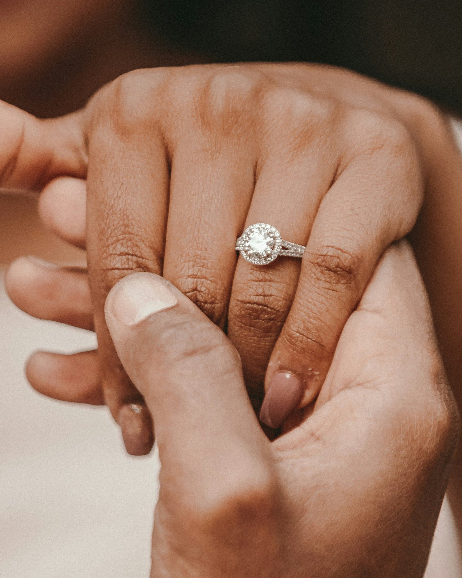 Close-up of two hands holding each other with a diamond ring on one finger.