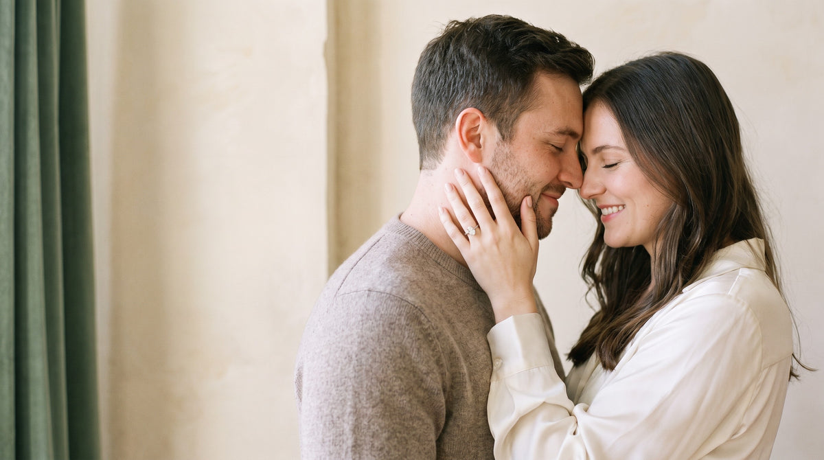 Couple in a tender embrace, her hand on his cheek showing an oval lab-grown diamond engagement ring | BEUSÉA
