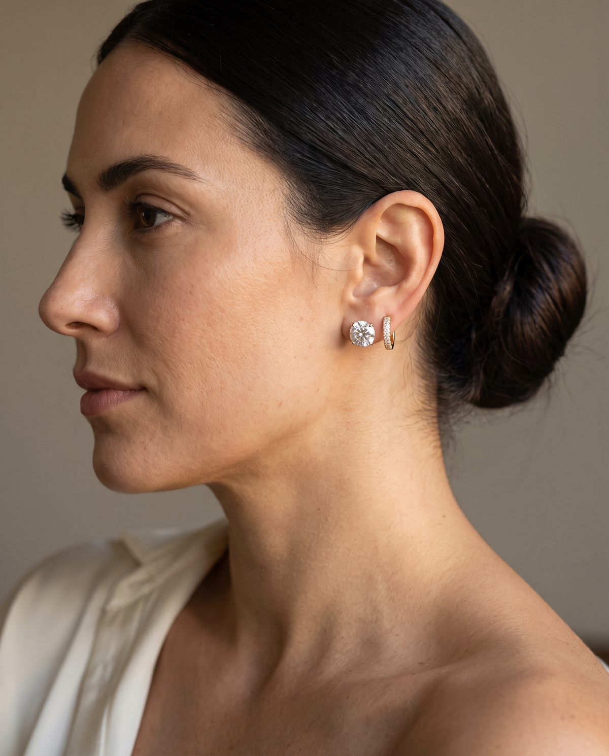Woman in profile wearing a diamond stud and diamond huggie hoop in yellow gold