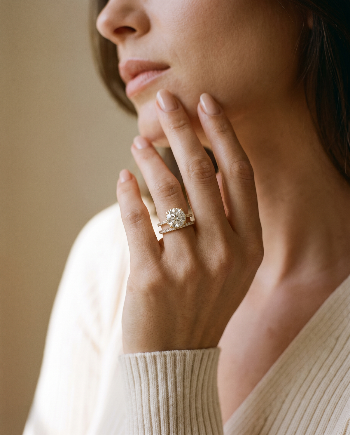 Hand at the chin wearing a hidden halo diamond engagement ring with a wedding band