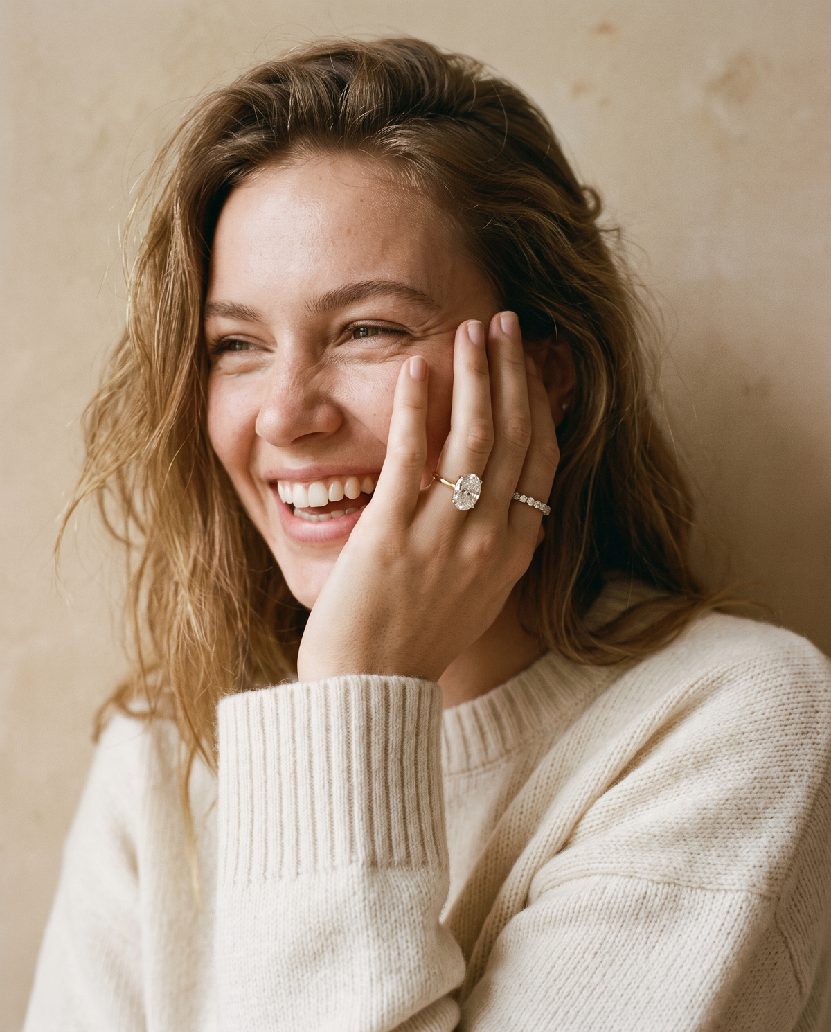 Woman smiling wearing an oval lab-grown diamond engagement ring and eternity band in yellow gold