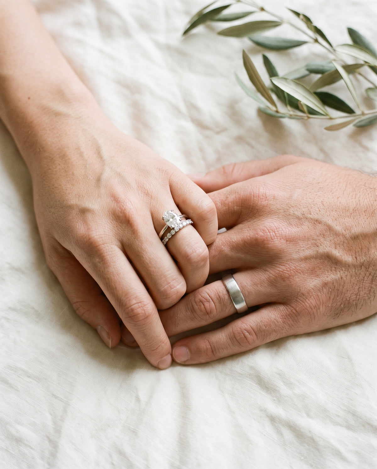 Couple holding hands wearing a diamond eternity band, oval engagement ring and platinum wedding band | BEUSÉA