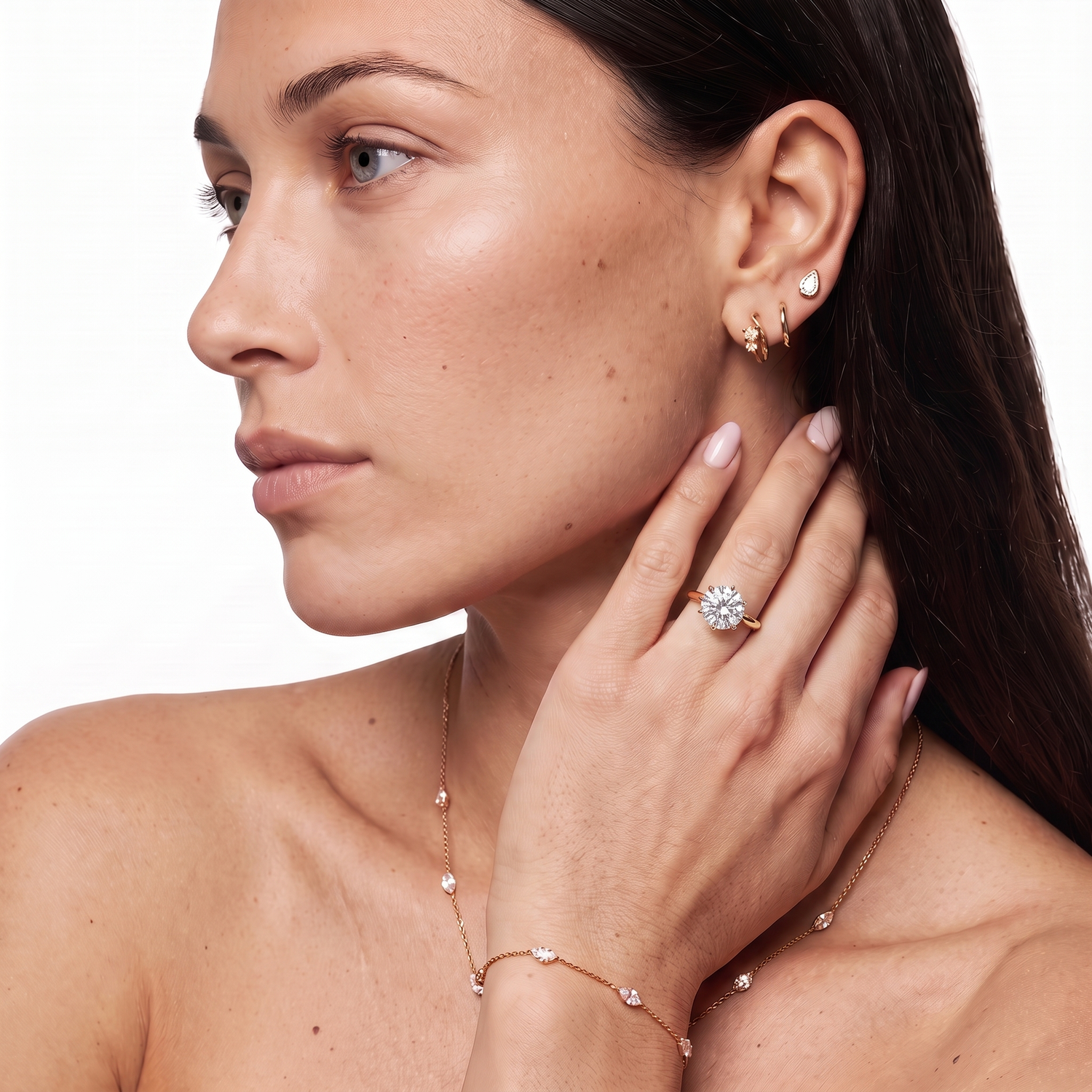 A close-up of a woman wearing a rose gold ring with a clear gemstone, a matching rose gold necklace, and a rose gold bracelet against a clean white background. 