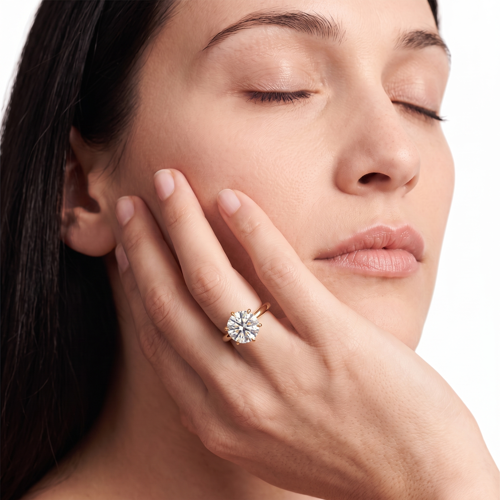 A close-up lifestyle shot of a woman with her eyes closed, resting her hand on her cheek, wearing a rose gold ring with a clear round-cut gemstone. 
