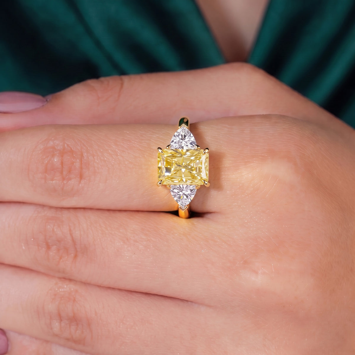 Fancy Vivid Yellow radiant lab-grown diamond three-stone ring with trillion side diamonds in 18K (750) rose gold, worn on finger, on-hand top view 